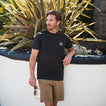 Man wearing black Shells Tee facing left outdoors, showcasing comfort-focused apparel for beach-inspired lifestyle.