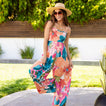 Woman wearing Eve Wide Leg Romper with colorful floral pattern, smiling outdoors in sun hat and sunglasses.