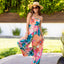 Woman wearing Eve Wide Leg Romper with colorful floral pattern, smiling outdoors in sun hat and sunglasses.