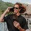 Man holding a pair of Leather Offshore sandals, one facing forward and the other showing the outsole, beach background.