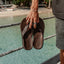 Leather Offshore men's dark brown sandals held by hand showing top view with cushioned footbed by the water.