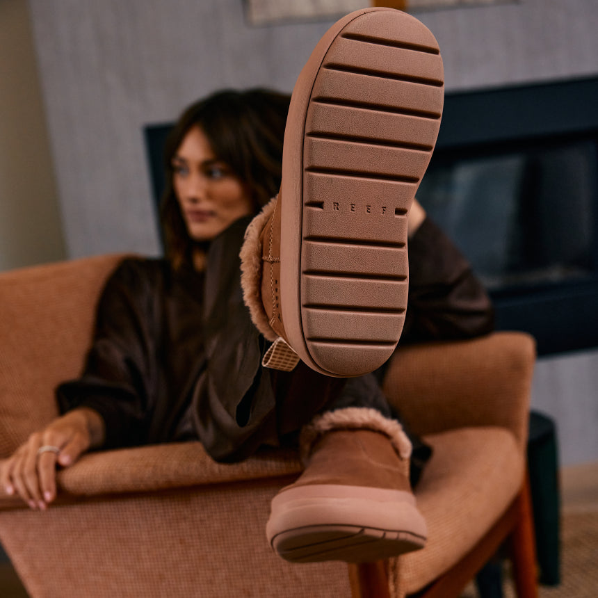 Close-up of brown REEF boots with soles facing the camera as a woman sits in a chair