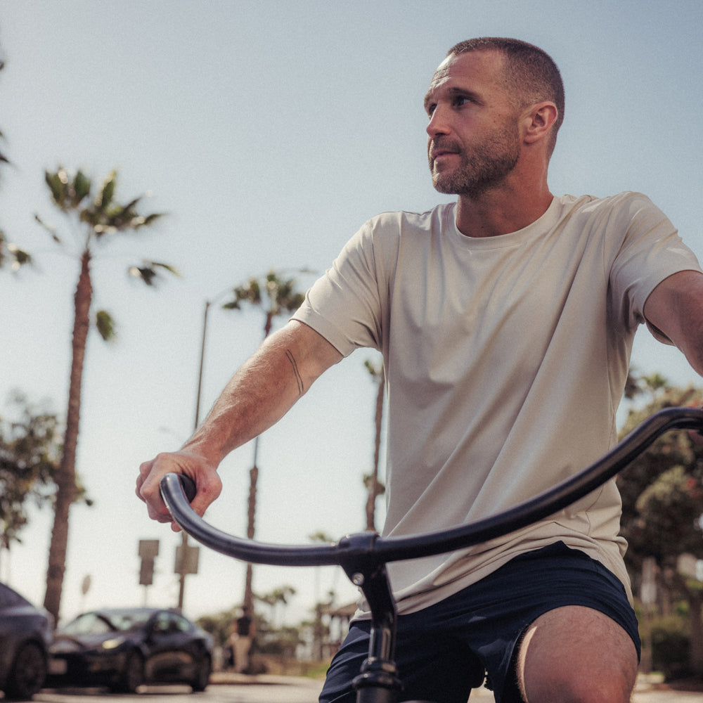 Man riding a bicycle outdoors with palm trees and cars in the background
