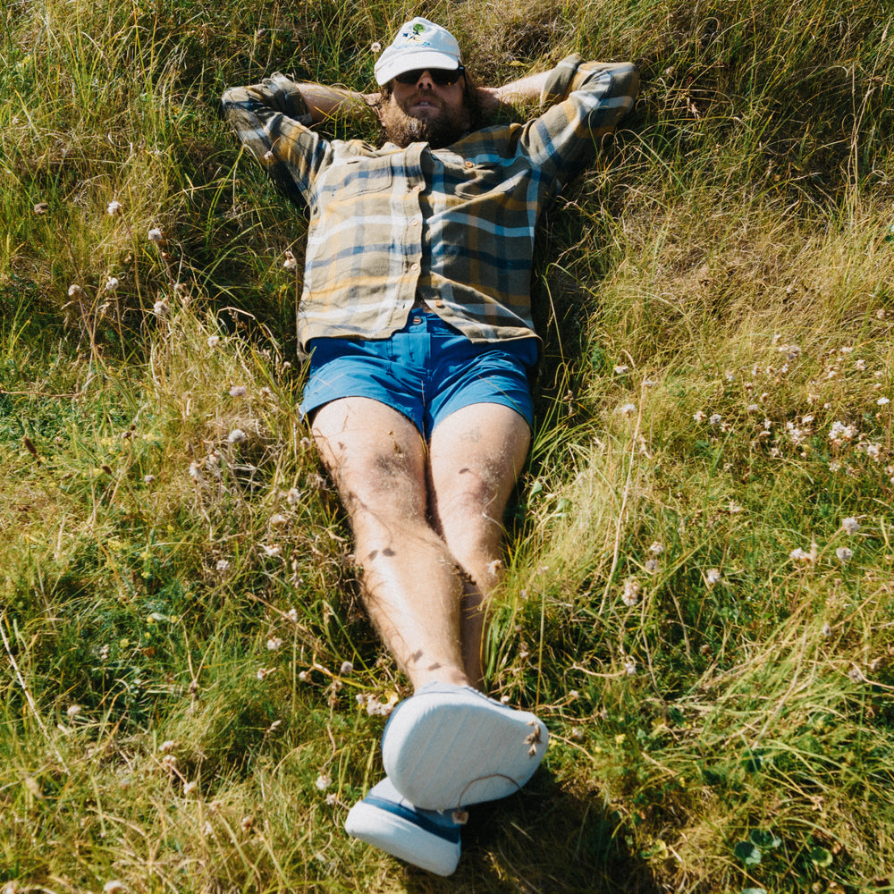Man reclining in tall grass with the soles of his light-colored sneakers facing the camera