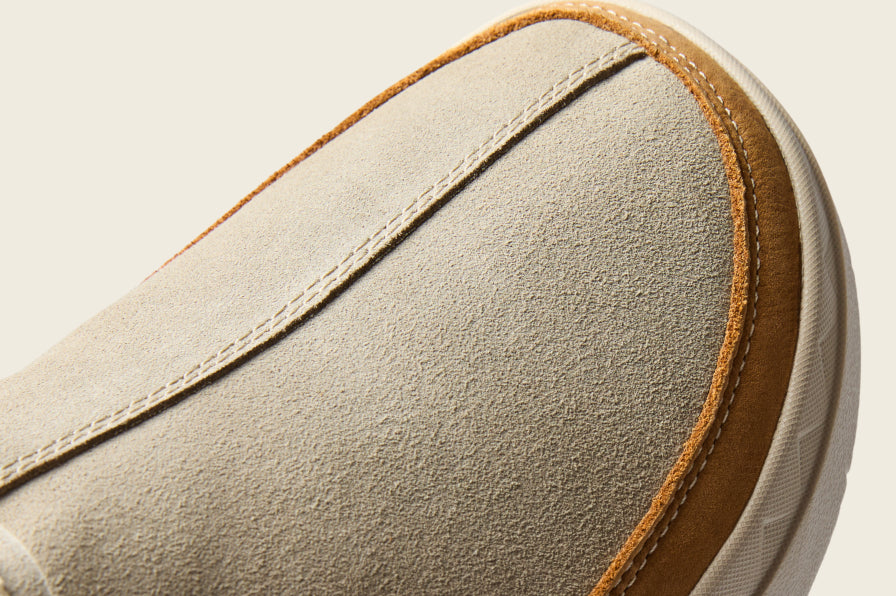 Close up of a beige shoe facing left showing its stitched toe and textured upper