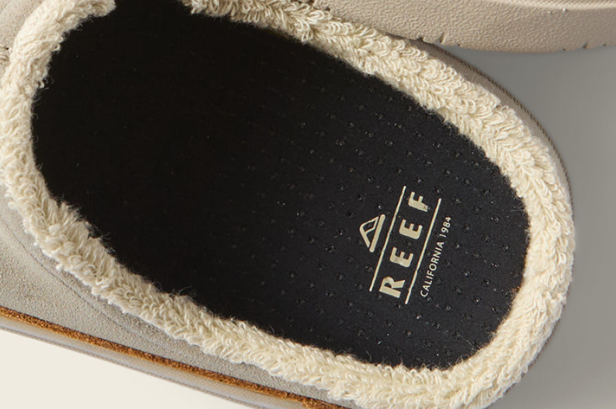 Close-up of a REEF sandal footbed facing upward, with black cushioning and cream fabric trim
