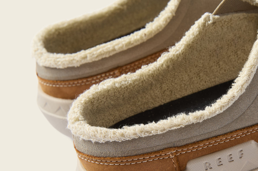 Close-up of tan fleece-lined slip-on shoes facing left, showing plush collars and stitched leather sides