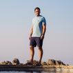 Man wearing La Loca Tee in light blue, standing outdoors in beach-inspired casual apparel with sandals facing forward.