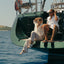Woman wearing white Reef Water Vista sandals facing forward while sitting on a boat, showcasing water-friendly comfort and style.