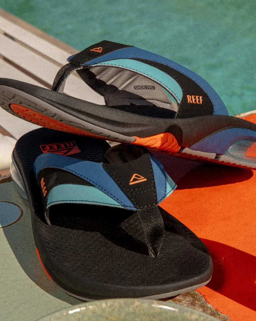 Pair of black, blue, and orange flip flops by a pool