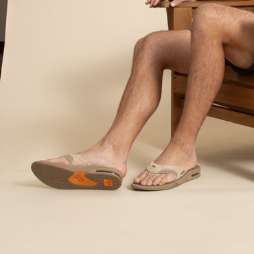 Fanning men's tan flip flop facing left with close-up on footbed and soft-rebound cushioning, surf-inspired comfort.