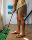 Man wearing Men's Reverb Short Unlined – 7" - Coconut with tan sandals facing right indoors playing mini golf on green mat