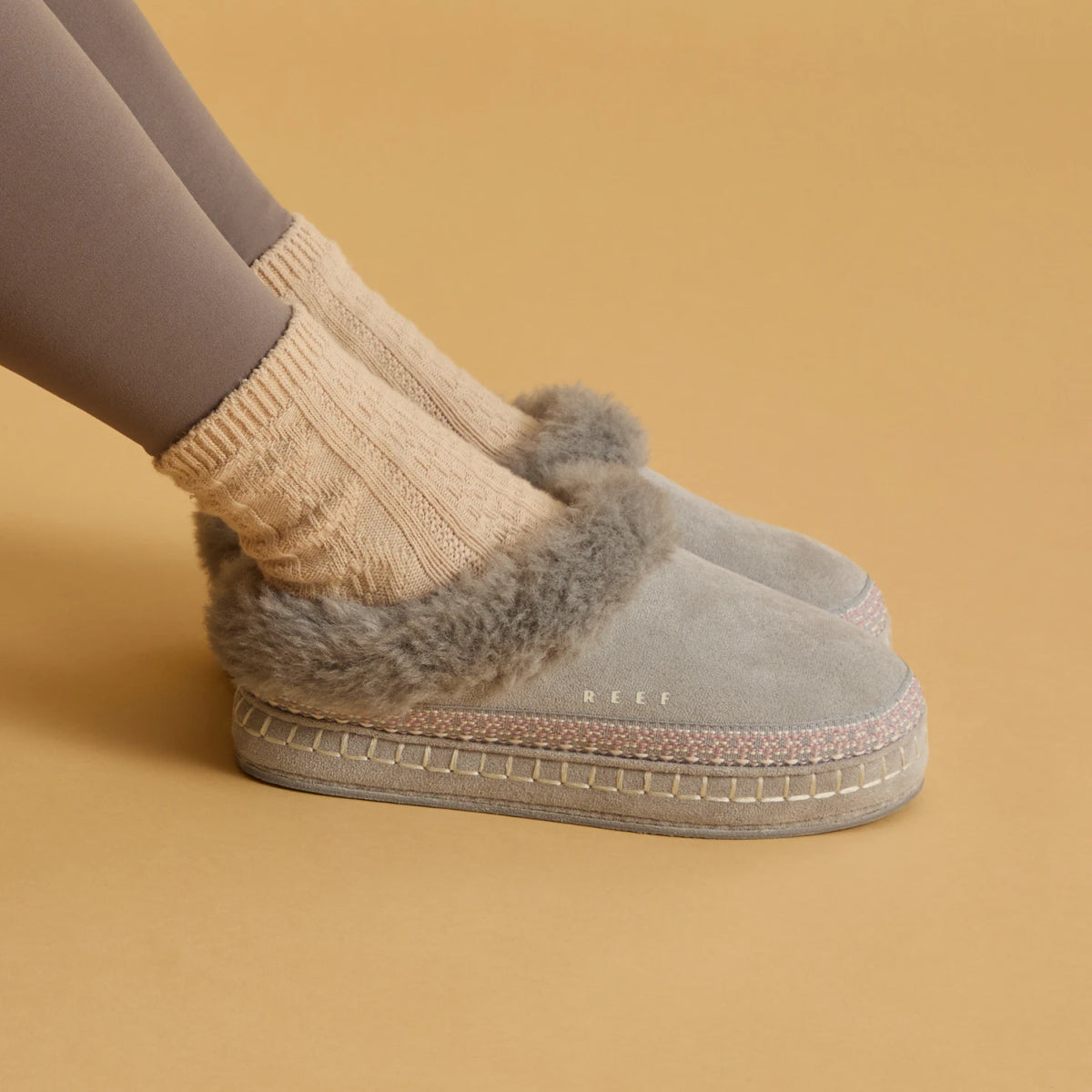 Close-up side view of a gray fuzzy-lined clog facing right, worn with a beige knit sock