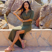 Woman wearing olive Up North Sweater Top seated outdoors showing front and side view with pink comfort sandals facing right