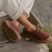 Burgundy slip-on shoes on a wooden deck, one facing right and the other showing its textured outsole