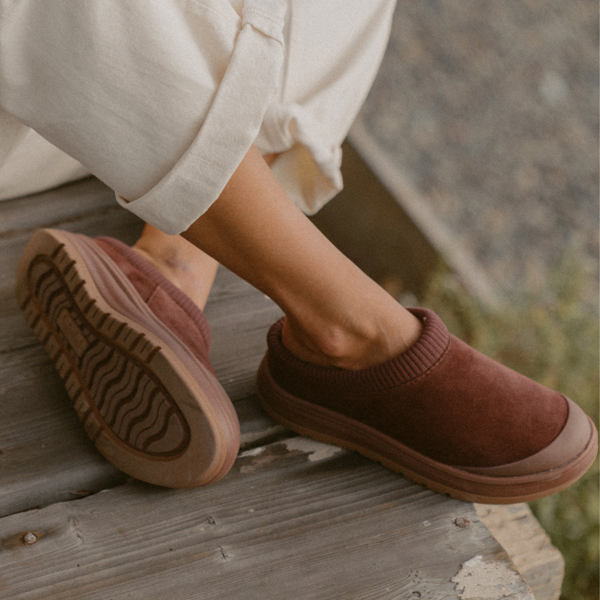 Burgundy slip-on shoes on a wooden deck, one facing right and the other showing its textured outsole