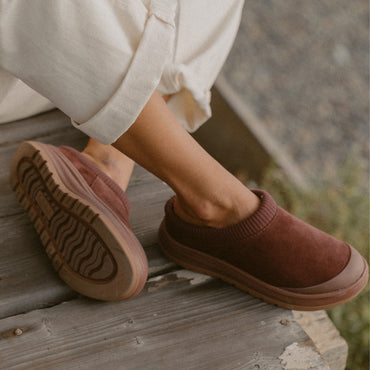 Burgundy slip-on shoes on a wooden deck, one facing right and the other showing its textured outsole