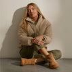 Woman seated against a wall wearing tan ankle boots with toes facing forward and slightly outward