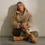 Woman seated against a wall wearing tan ankle boots with toes facing forward and slightly outward