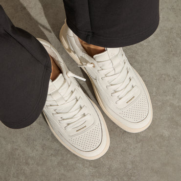 Kickback white sneakers facing lower right, top down close up of perforated toe boxes, laces, and cushioned soles
