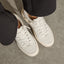 Kickback white sneakers facing lower right, top down close up of perforated toe boxes, laces, and cushioned soles