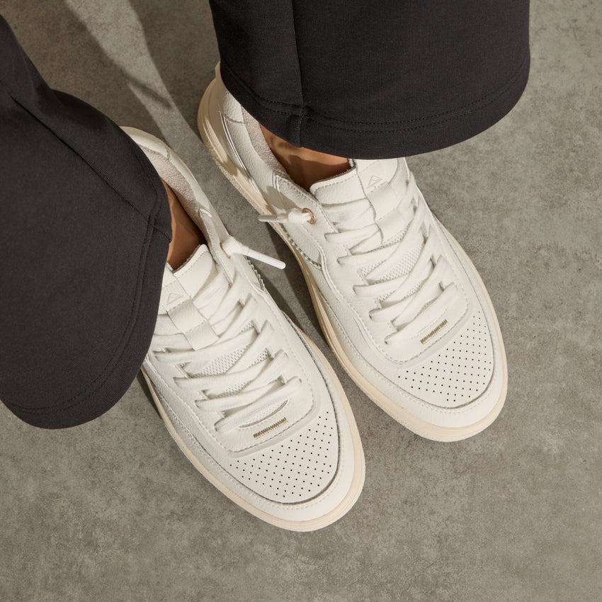 Kickback white sneakers facing lower right, top down close up of perforated toe boxes, laces, and cushioned soles