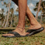 Cruiser men's black sandal facing right, close-up of footbed and arch support, beach background with palm trees.