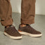 Pair of brown sneakers facing right, worn with cuffed brown pants on a concrete floor