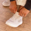 Close-up of a white sneaker facing lower left as hands adjust its laces.