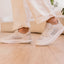 White sneakers worn indoors, with one shoe facing left and the other facing right, shown from the side