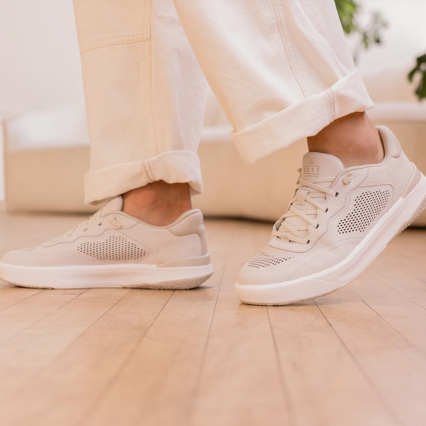 White sneakers worn indoors, with one shoe facing left and the other facing right, shown from the side