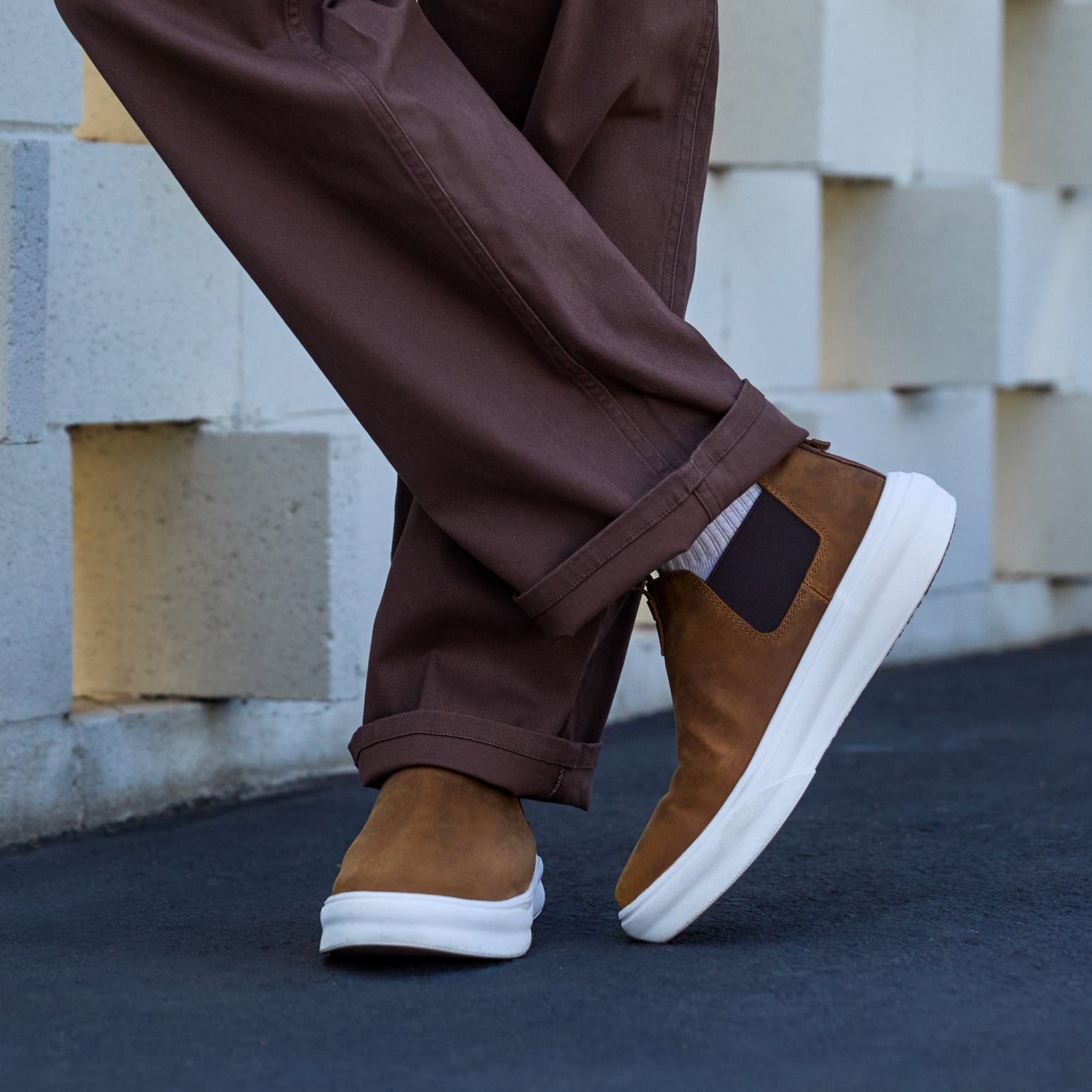 Evo mid-cut brown leather-look shoe facing right, worn with cuffed pants on outdoor pavement, comfort and style blend.