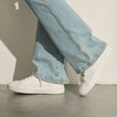 White knit sneakers facing left, worn with light blue jeans on a concrete floor
