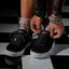 Lay Day Dawn black sneakers facing forward with hands adjusting the laces for comfortable everyday wear