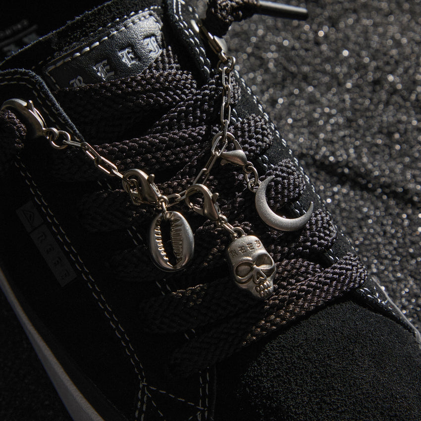 Close up of Lay Day Dawn black sneaker facing lower right showing the laces tongue and decorative charms