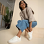 Woman wearing Lay Day Dawn white suede sneakers facing left, seated with a smile, showcasing comfort and casual style