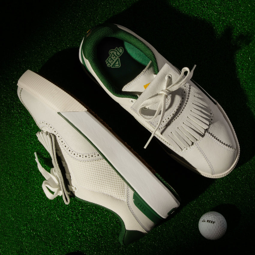Top and side view of white and green Onshore Pebble men's shoes on green turf with a REEF golf ball nearby