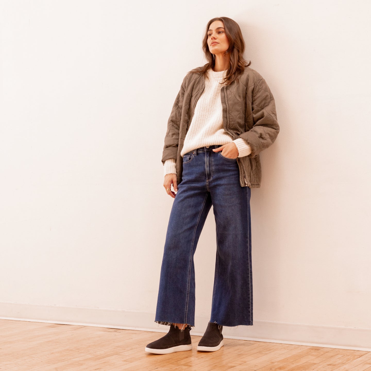 Woman standing wearing Neptune Athena black slip-on shoes facing left, styled with casual denim and jacket.