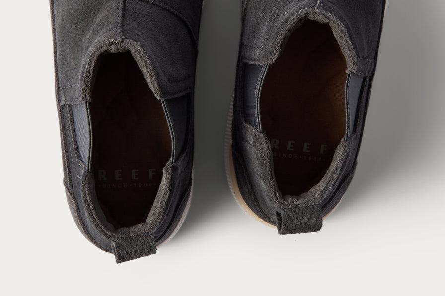Top view close-up of black REEF slip-on shoes showing cushioned footbeds and heel tabs for easy wear.