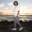 Man wearing Shorebreak TRV shoes facing left in grey walking pants, standing on rocky beach at sunset with ocean background.