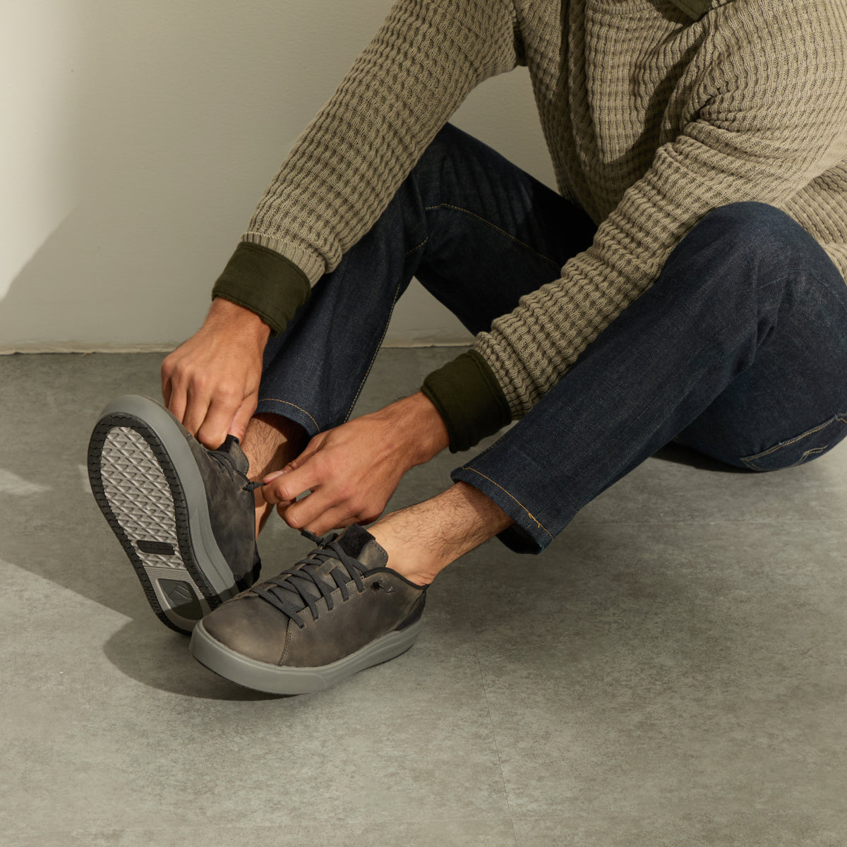 Person tying gray sneakers facing forward while seated on a concrete floor
