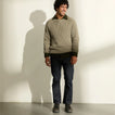 Man standing in a textured sweater and jeans wearing dark boots facing forward slightly outward