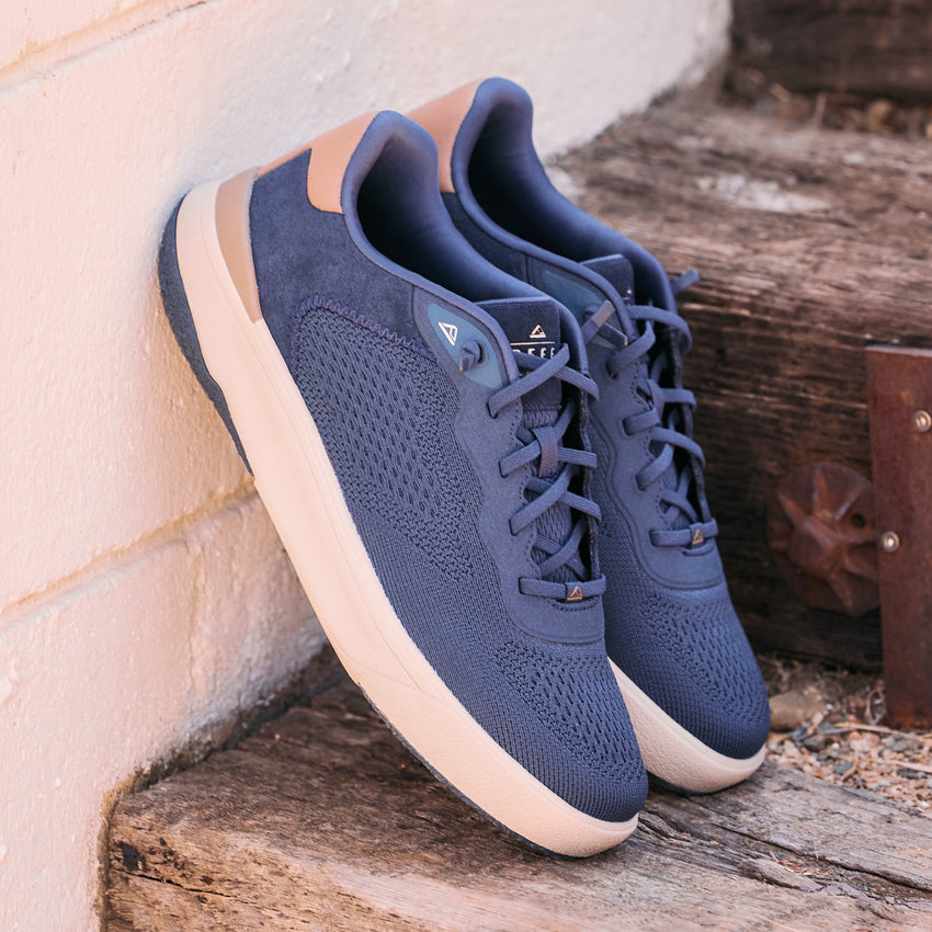 Pair of navy blue lace-up sneakers facing toward the lower right on a weathered wooden step