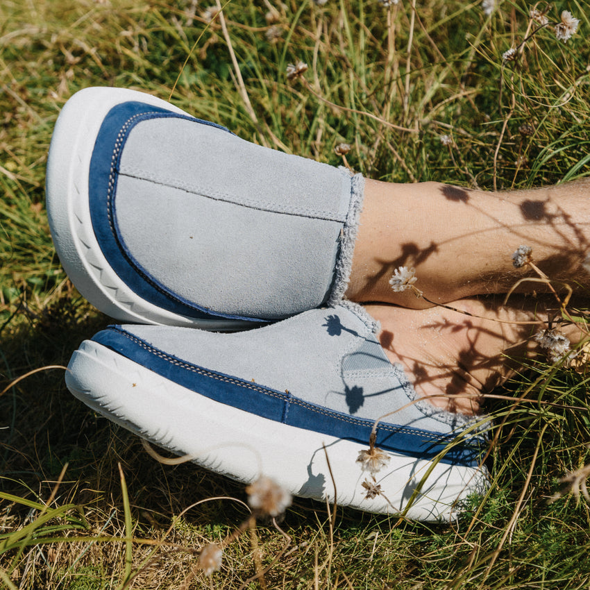 Blue and gray slip-on shoes facing left on feet resting in grassાન્ય