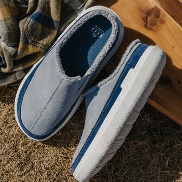 Close-up of gray and blue slip-on shoes, toes facing lower left and upper right, showing cushioned footbeds and side profile.