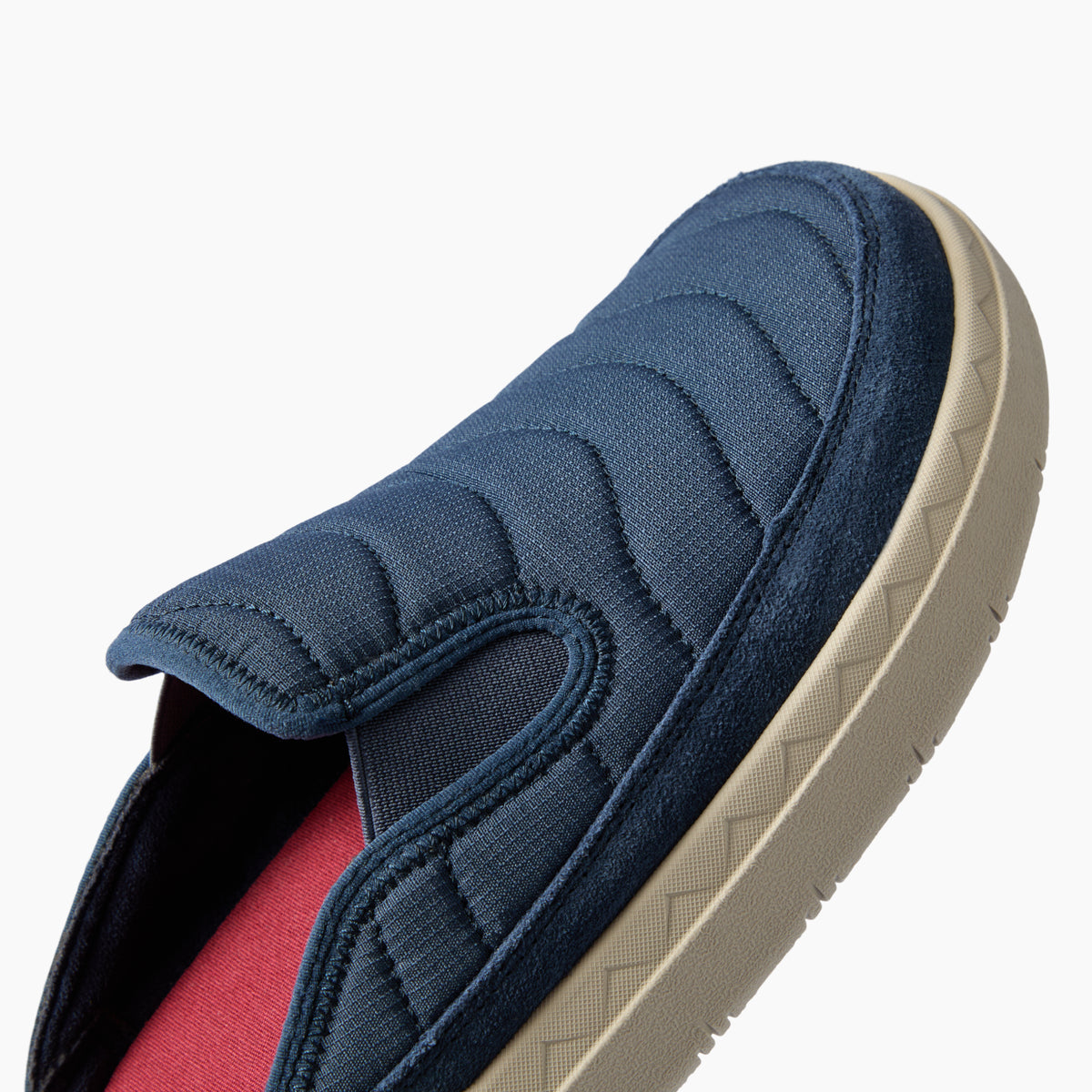 Navy slip-on shoe facing upper right, close-up of quilted upper, side profile, and textured cushioned sole