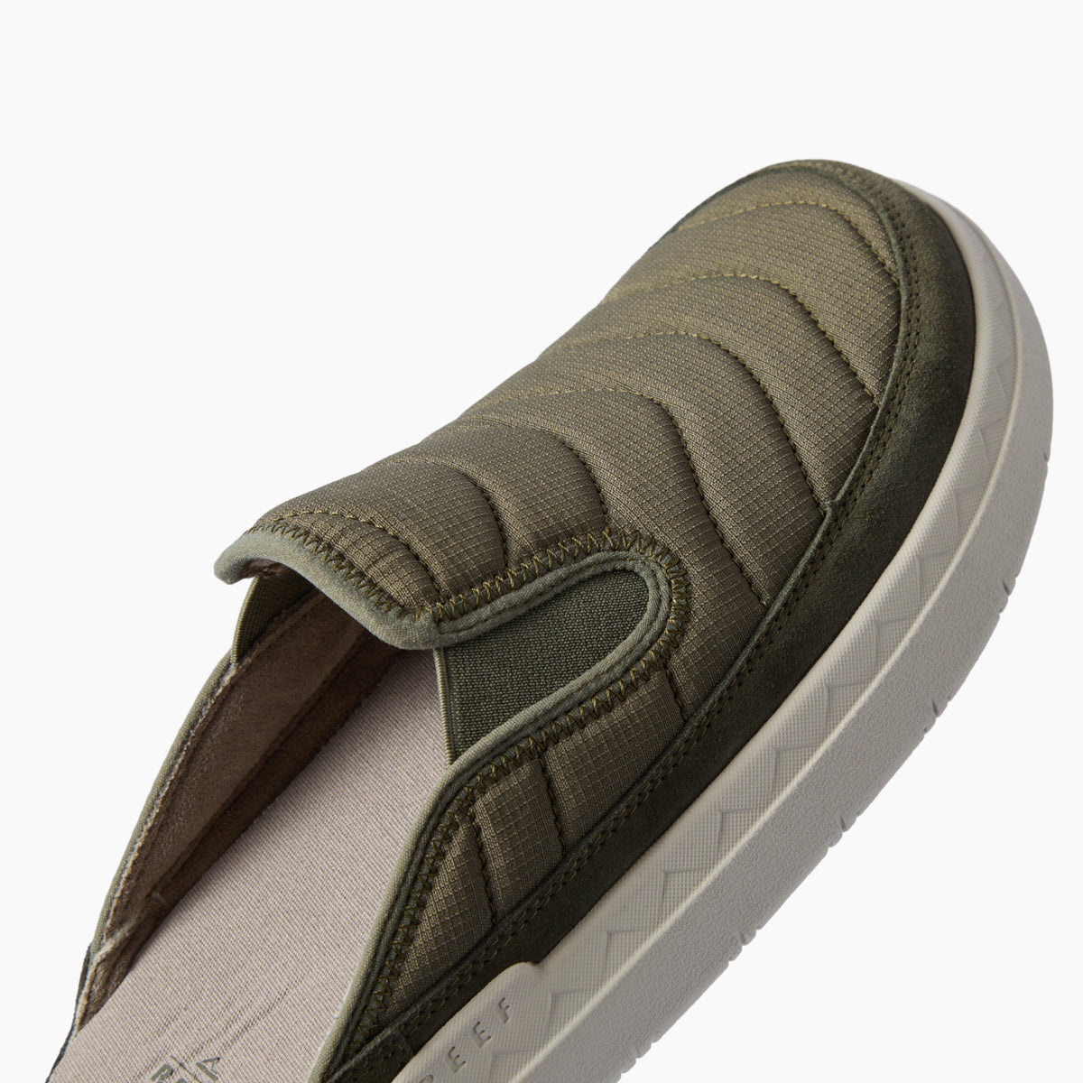 Olive slip on shoe facing upper right with a close up of its padded quilted upper and textured sole