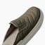 Olive slip on shoe facing upper right with a close up of its padded quilted upper and textured sole