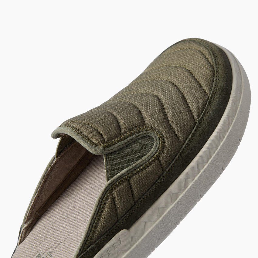 Olive slip on shoe facing upper right with a close up of its padded quilted upper and textured sole