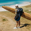 Rambler shoes facing left on a beach trail with a surfboard and backpack